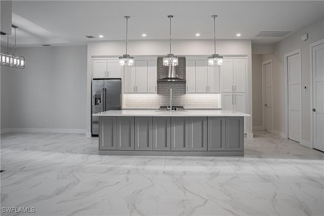 kitchen with light countertops, stainless steel fridge, wall chimney range hood, and decorative backsplash