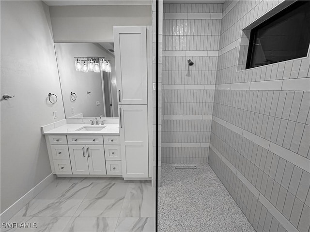 full bath featuring marble finish floor, tiled shower, vanity, and baseboards