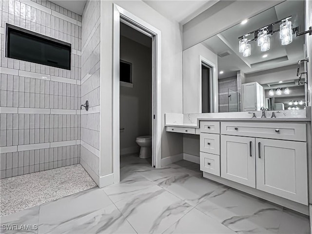 bathroom featuring marble finish floor, toilet, a tile shower, vanity, and baseboards