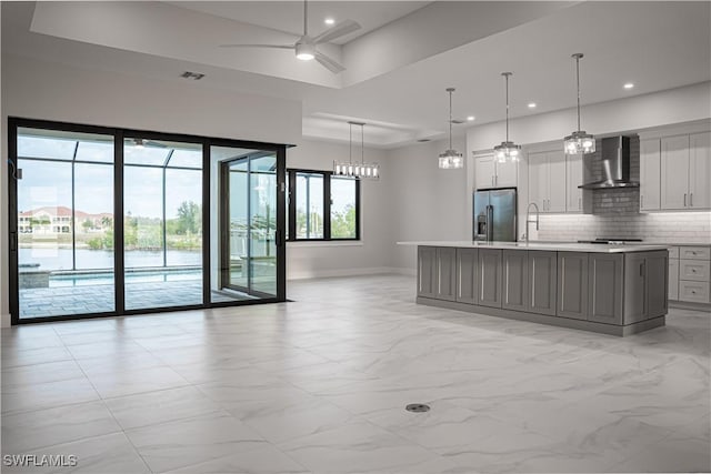 kitchen featuring stainless steel refrigerator with ice dispenser, tasteful backsplash, light countertops, ceiling fan, and wall chimney range hood