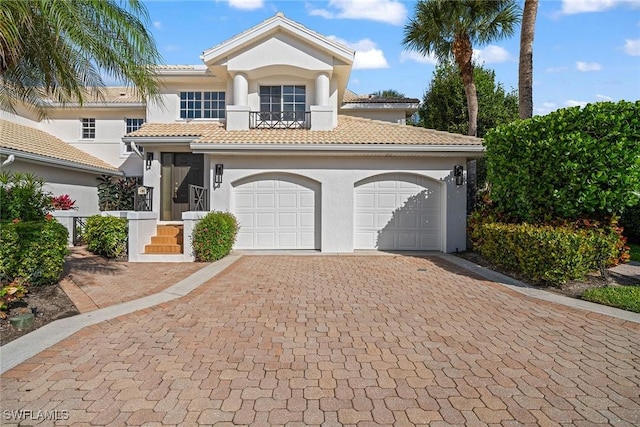 mediterranean / spanish-style house with a garage, decorative driveway, a tile roof, and stucco siding