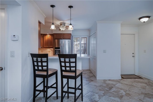 kitchen featuring stainless steel fridge, a breakfast bar, brown cabinets, light countertops, and hanging light fixtures