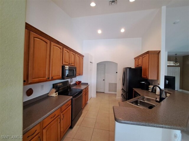 kitchen featuring arched walkways, dark countertops, a sink, a peninsula, and black appliances