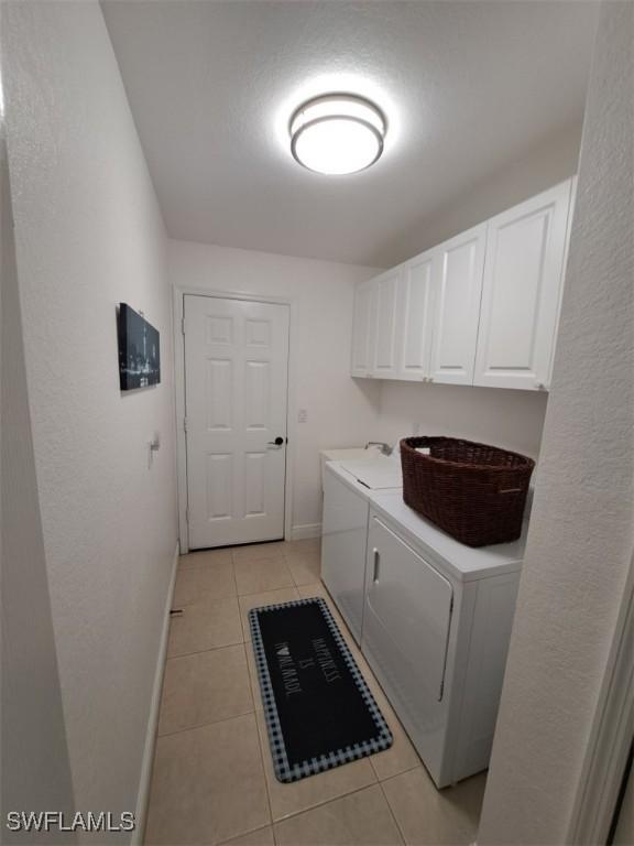 laundry area with light tile patterned flooring, washing machine and dryer, cabinet space, and baseboards