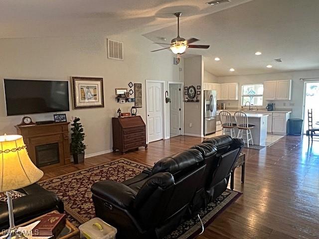 living room with dark wood-style flooring, a fireplace, visible vents, a ceiling fan, and vaulted ceiling