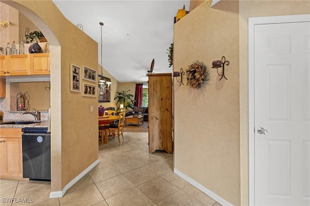 corridor featuring light tile patterned floors, baseboards, arched walkways, and a sink