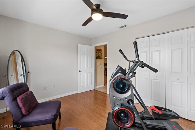 exercise room with a ceiling fan, visible vents, baseboards, and wood finished floors