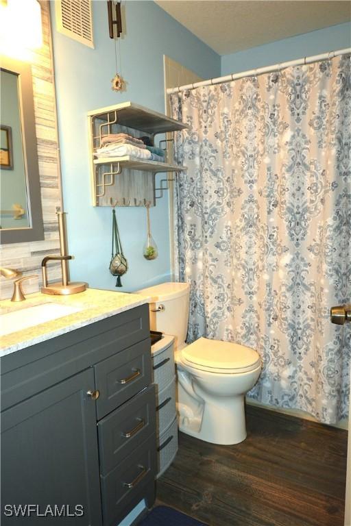 full bath featuring visible vents, toilet, curtained shower, wood finished floors, and vanity