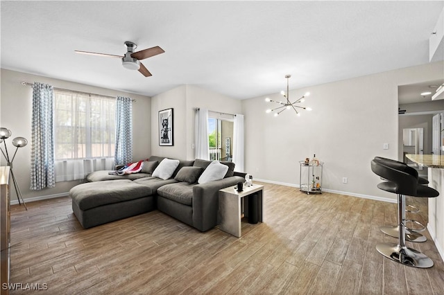 living room featuring light wood-style flooring, baseboards, and ceiling fan with notable chandelier