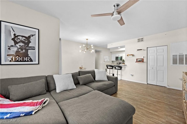 living area with ceiling fan with notable chandelier, wood finished floors, visible vents, and baseboards