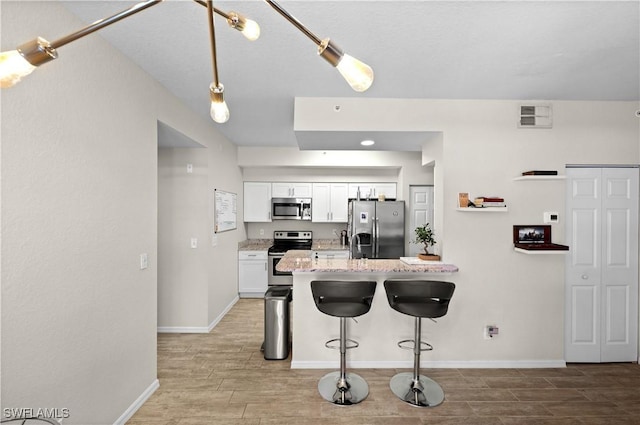 kitchen with visible vents, appliances with stainless steel finishes, white cabinets, a peninsula, and a kitchen bar