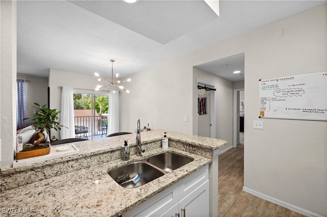 kitchen featuring baseboards, light wood-style flooring, light stone countertops, white cabinetry, and a sink