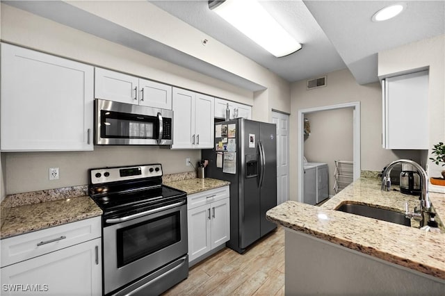 kitchen featuring light stone counters, washer and clothes dryer, light wood finished floors, stainless steel appliances, and a sink