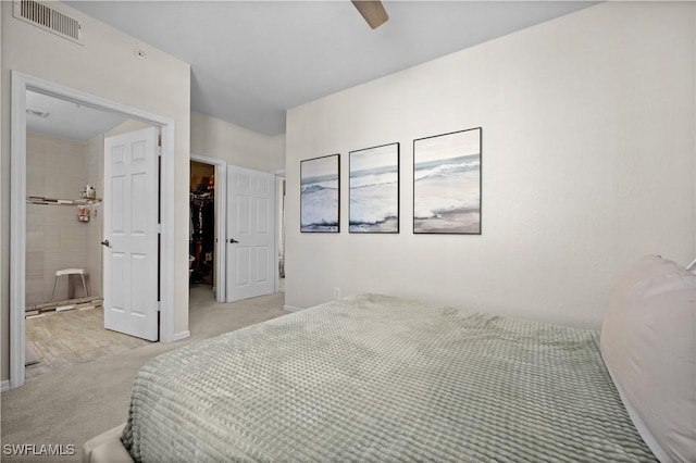 bedroom with light colored carpet, visible vents, a closet, a walk in closet, and ensuite bath