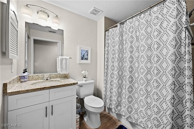 bathroom featuring visible vents, a textured wall, toilet, vanity, and wood finished floors