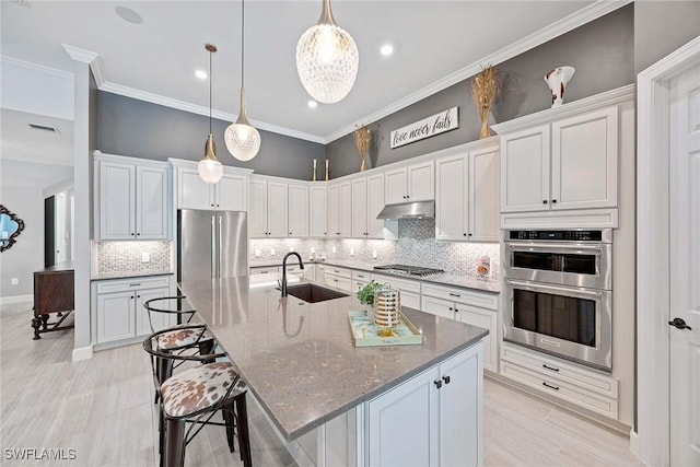 kitchen featuring visible vents, a large island, ornamental molding, stainless steel appliances, and a sink