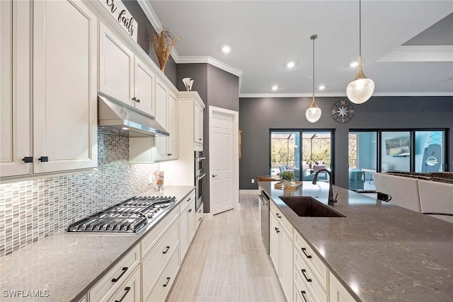 kitchen featuring stainless steel appliances, ornamental molding, a sink, dark stone counters, and under cabinet range hood