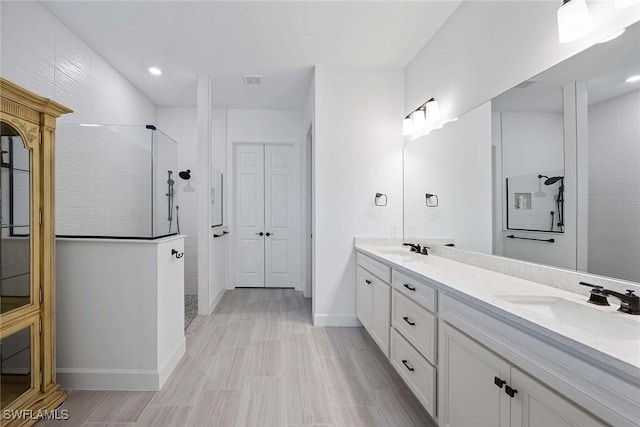 bathroom featuring a walk in shower, double vanity, a sink, and baseboards