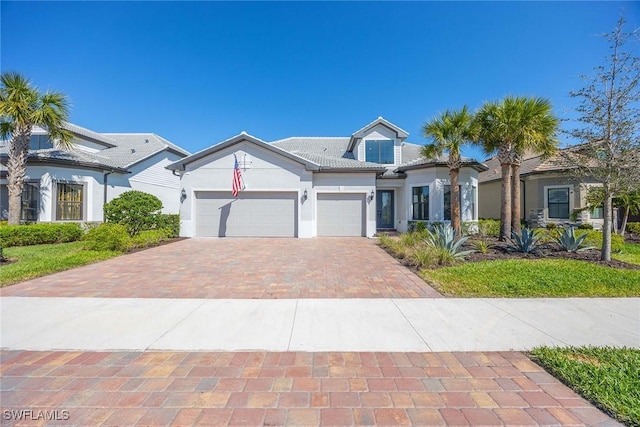 view of front facade featuring a garage, decorative driveway, a tile roof, and stucco siding