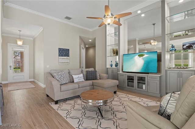 living area featuring visible vents, light wood-style floors, ornamental molding, ceiling fan, and baseboards