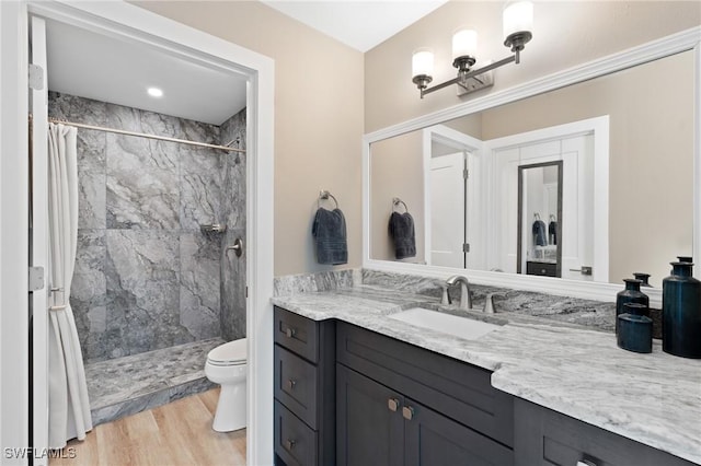 full bath featuring a tile shower, vanity, toilet, and wood finished floors