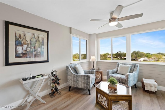 living area featuring baseboards, ceiling fan, and light wood finished floors