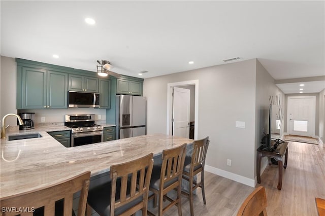 kitchen with light stone counters, a sink, visible vents, appliances with stainless steel finishes, and green cabinetry