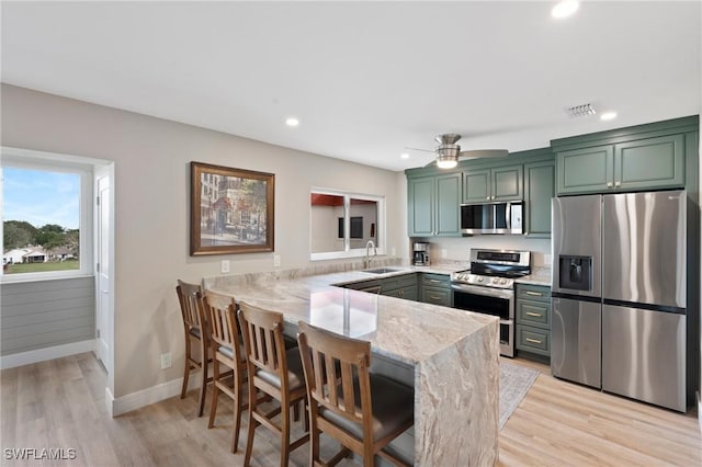 kitchen with light wood finished floors, stainless steel appliances, a sink, light stone countertops, and a peninsula