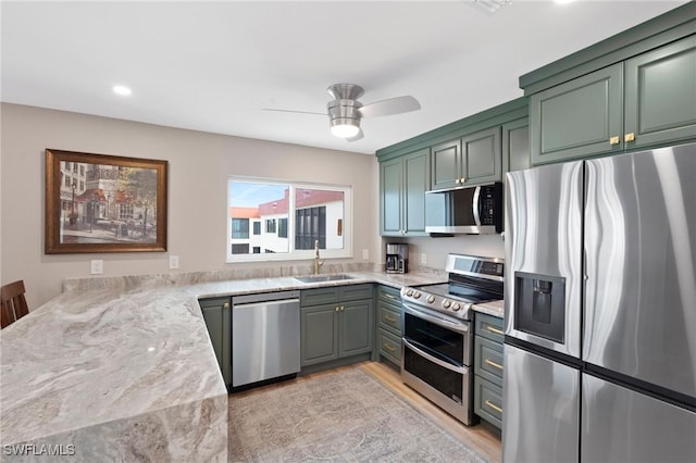 kitchen featuring a ceiling fan, light wood-style flooring, appliances with stainless steel finishes, green cabinets, and a sink