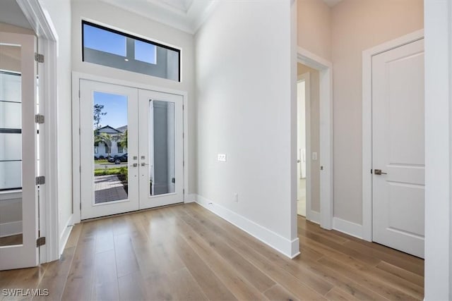 entryway with french doors, light wood-type flooring, a towering ceiling, and baseboards