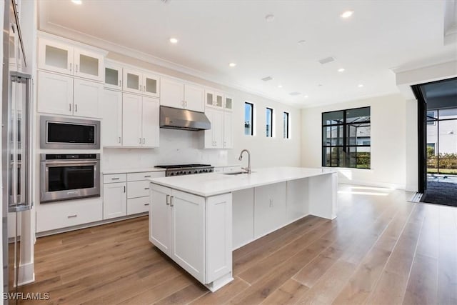 kitchen with light wood finished floors, light countertops, stainless steel appliances, crown molding, and under cabinet range hood