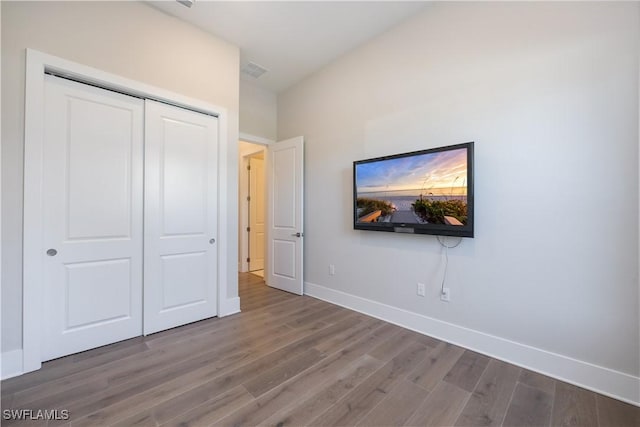 unfurnished bedroom featuring a closet, visible vents, baseboards, and wood finished floors