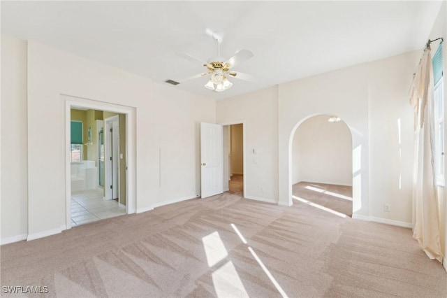 carpeted empty room featuring baseboards, visible vents, arched walkways, and a ceiling fan