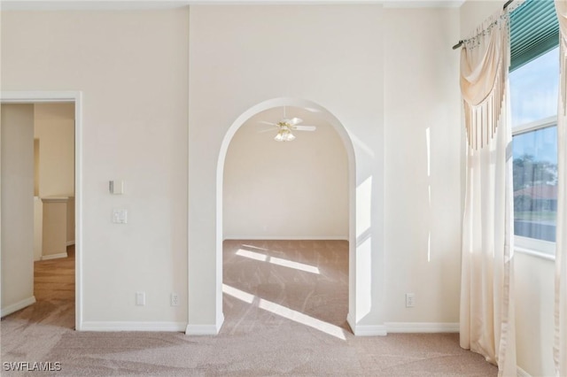 empty room featuring ceiling fan, carpet, arched walkways, and baseboards