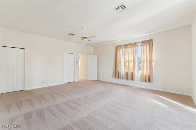 unfurnished bedroom featuring baseboards, carpet, visible vents, and multiple closets