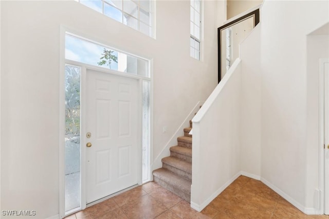 foyer entrance with a towering ceiling, stairway, baseboards, and tile patterned floors