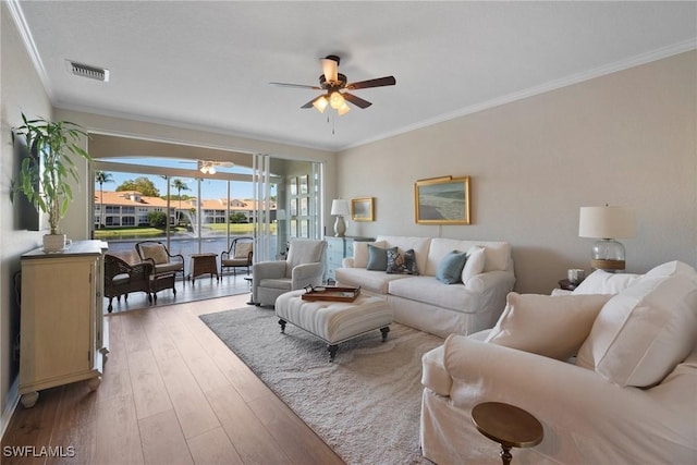 living room featuring a ceiling fan, visible vents, ornamental molding, and wood finished floors