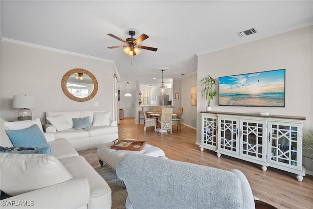 living room with ornamental molding, visible vents, ceiling fan, and wood finished floors