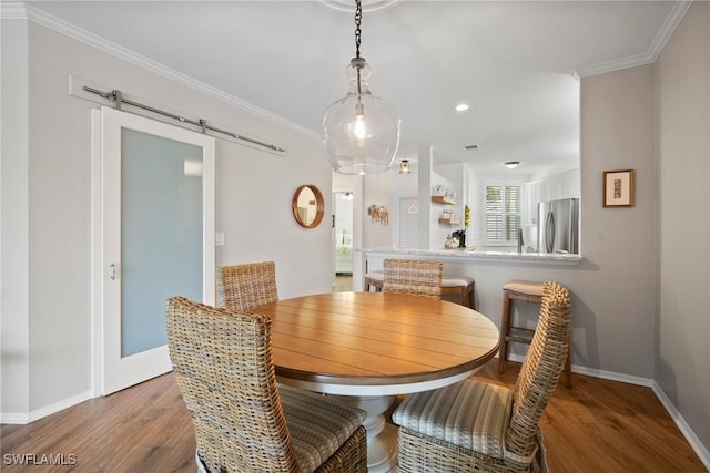 dining room featuring baseboards, a barn door, wood finished floors, and crown molding