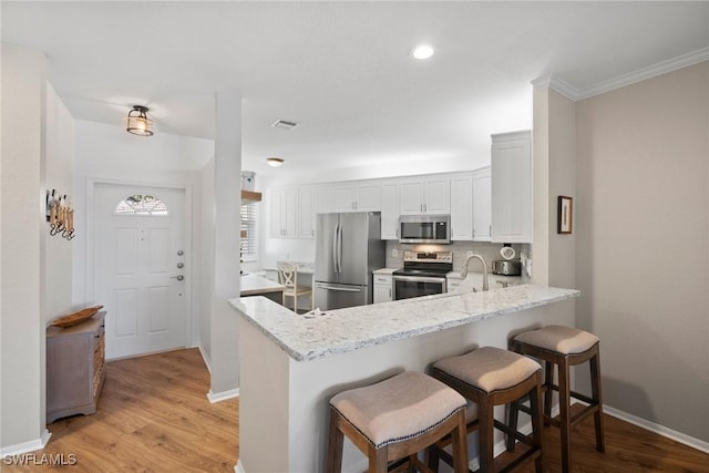 kitchen featuring a peninsula, white cabinetry, light wood-style floors, appliances with stainless steel finishes, and light stone countertops