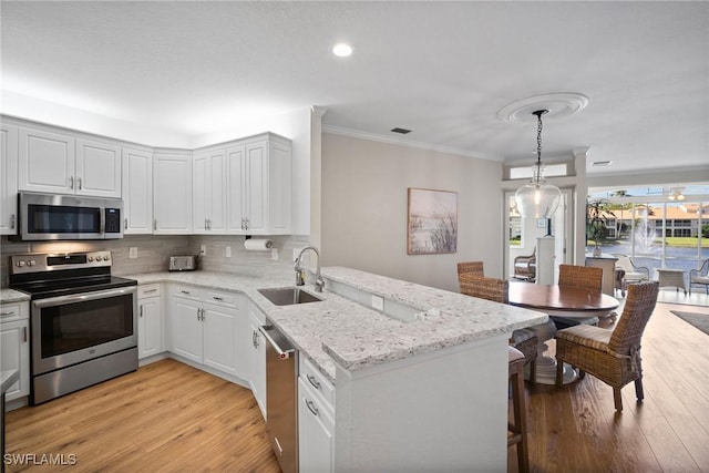 kitchen featuring stainless steel appliances, decorative backsplash, a sink, light wood-type flooring, and a peninsula