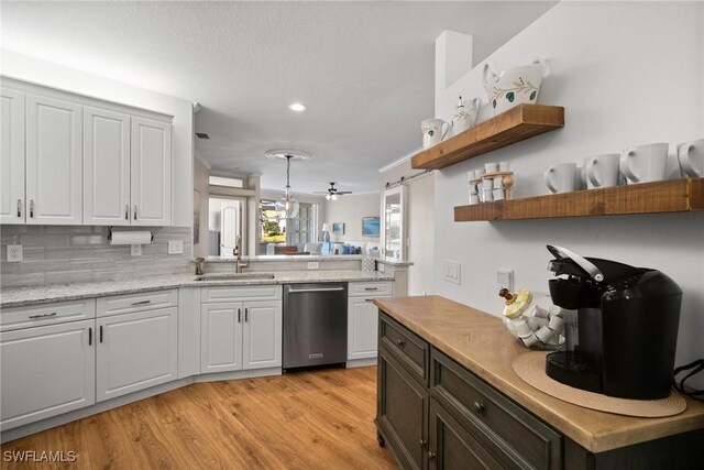 kitchen featuring a sink, stainless steel dishwasher, light wood-type flooring, decorative backsplash, and open shelves