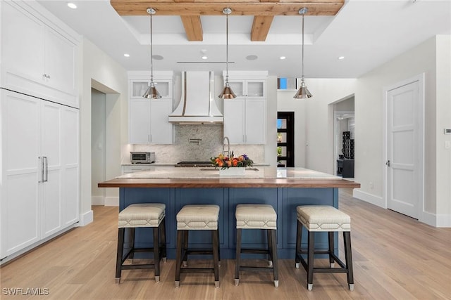 kitchen featuring light wood-style flooring, white cabinets, backsplash, custom exhaust hood, and beamed ceiling