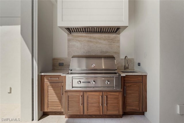 kitchen with tasteful backsplash, light countertops, brown cabinetry, a sink, and premium range hood