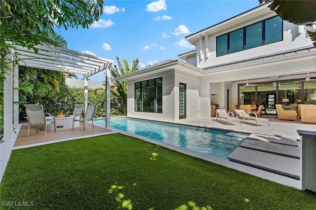 rear view of house featuring an outdoor pool, a yard, a wooden deck, a pergola, and stucco siding