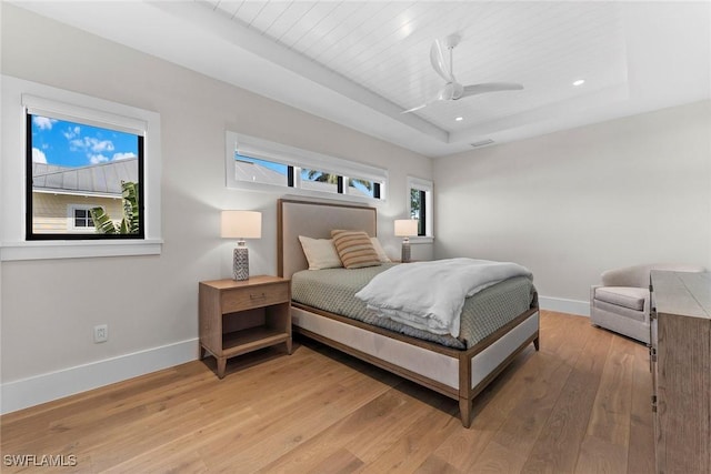 bedroom featuring light wood-style floors, a tray ceiling, multiple windows, and baseboards