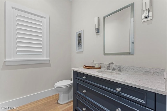 half bathroom featuring baseboards, vanity, toilet, and wood finished floors