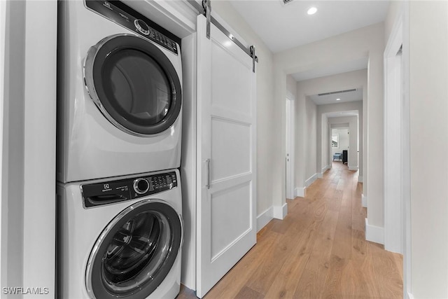 washroom with laundry area, a barn door, light wood finished floors, baseboards, and stacked washer and clothes dryer