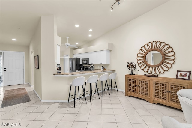 kitchen with appliances with stainless steel finishes, light tile patterned flooring, a kitchen bar, and white cabinetry