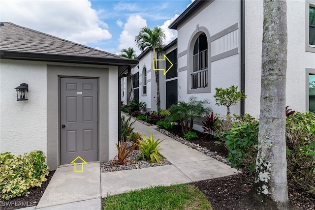 property entrance with a shingled roof and stucco siding